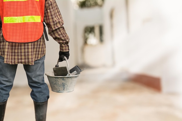 Foto mittelabschnitt eines arbeiters, der einen eimer mit handwerkzeugen auf einer baustelle hält