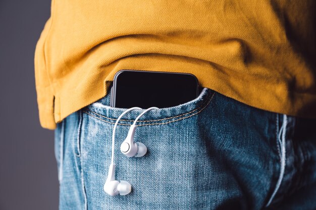 Mittelabschnitt eines Mannes mit Mobiltelefon und In-Ear-Kopfhörern in der Tasche