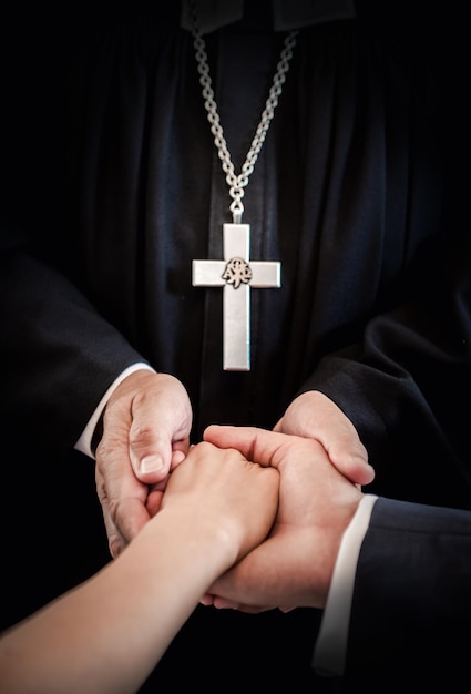 Mittelabschnitt eines Priesters, der während der Hochzeit ein Paar an der Hand hält