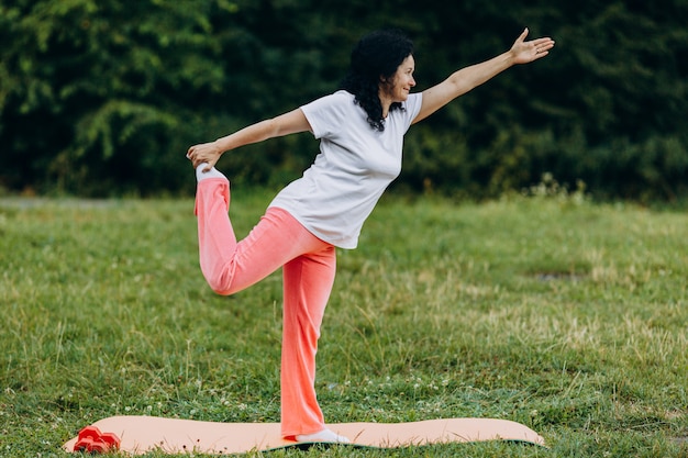 Mittelalterfrau, welche die Yogahaltung hält ihr Bein im Freien tut. Sport