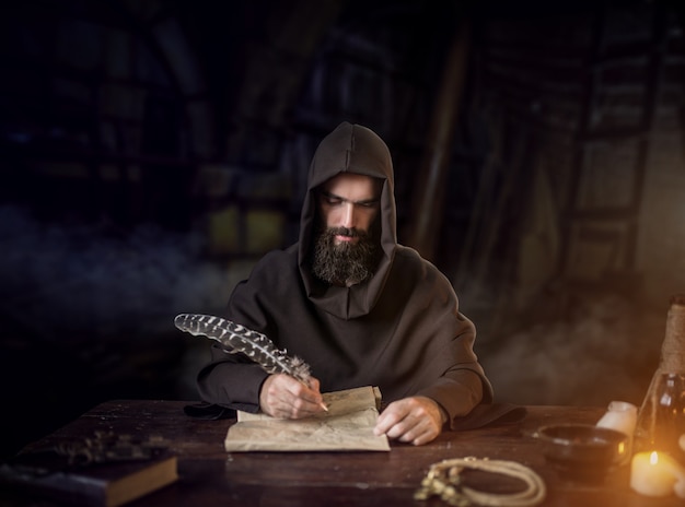 Mittelalterlicher Mönch in Robe schreibt mit einer Gänsefeder