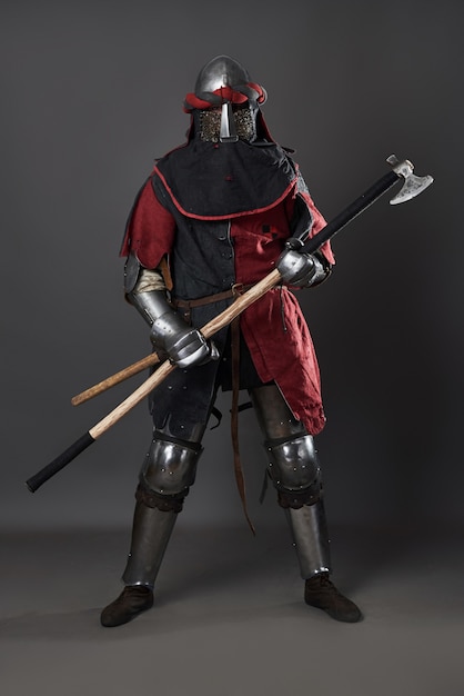 Mittelalterlicher Ritter auf grauem Hintergrund. Porträt eines brutalen schmutzigen Gesichtskriegers mit roter und schwarzer Kleidung der Kettenhemdrüstung und Streitaxt.