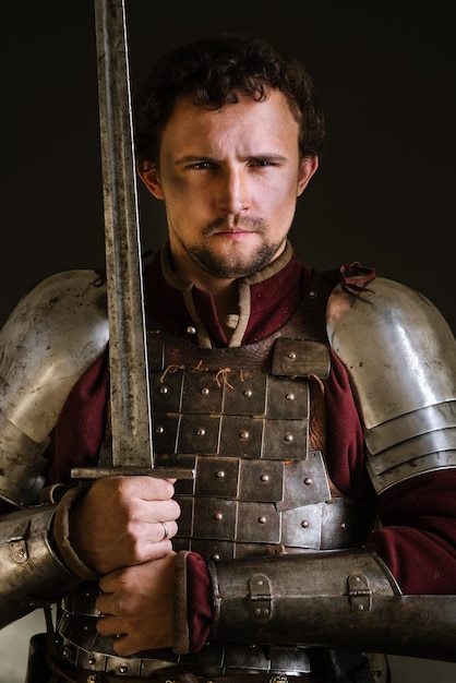 Mittelalterlicher Ritter in Rüstung und Waffe auf dunklem Hintergrund. Porträt des Ritters