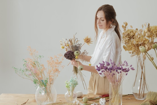 Mittelgroße Frau, die mit getrockneten Blumen arbeitet, stellt Kompositionsdekor und Floristikkonzept zusammen