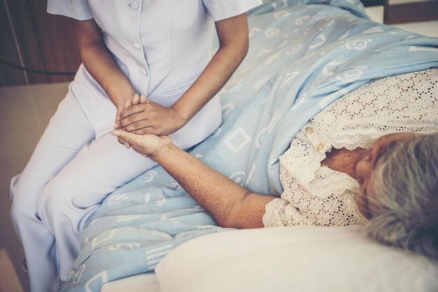 Foto mittelschnitt einer krankenschwester, die die hand einer älteren patientin hält, die sich im krankenhaus auf dem bett entspannt