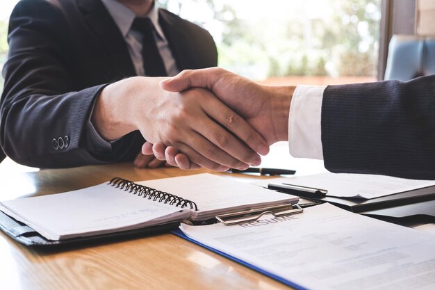 Foto mittelschnitt eines kandidaten, der sich während des interviews im büro mit einem geschäftsmann die hand schüttelt