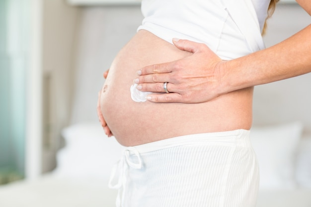 Mittelteil der Frau Creme auf Bauch anwendend