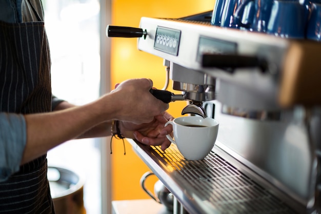 Mittelteil des Kellners, der eine Tasse Kaffee an der Theke macht