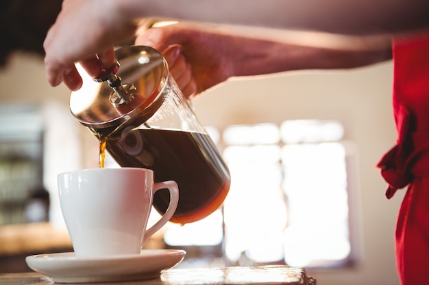 Mittelteil des Kellners, der eine Tasse Kaffee einschenkt