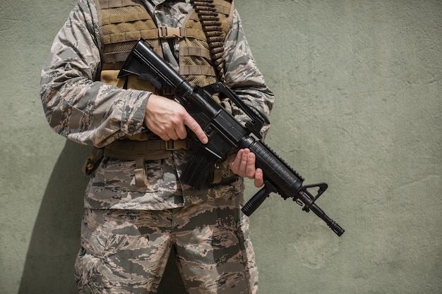 Mittelteil des Militärsoldaten, der mit einem Gewehr gegen Betonwand im Bootcamp steht