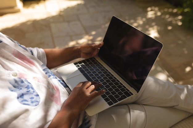 Mittelteil einer älteren afroamerikanischen Frau, die auf einer schattigen Terrasse im sonnigen Garten einen Laptop benutzt. Rückzug, Ruhestand und glückliches Senioren-Lifestyle-Konzept.
