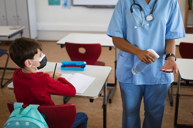 Mittelteil einer Gesundheitshelferin, die Schülern zeigt, wie sie in der Grundschule Händedesinfektionsmittel verwenden