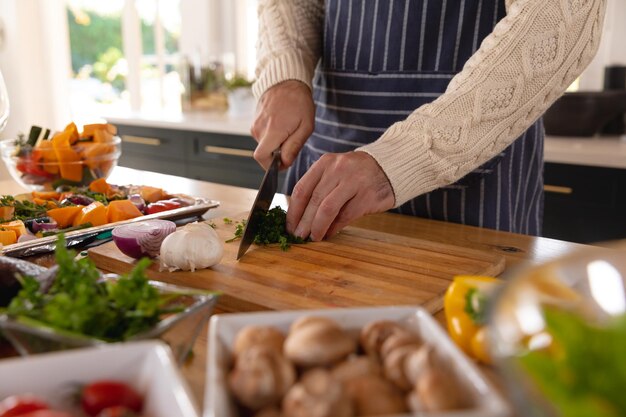 Mittelteil eines kaukasischen Mannes, der mit einer Schürze in der Küche Essen zubereitet und Gemüse hackt. Konzept für häusliches Leben, Freizeit, Gesundheit und Glück.