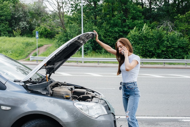 Mitten auf der Autobahn steht ein junges Mädchen neben einem kaputten Auto und ruft am Telefon um Hilfe. Ausfall und Panne des Autos. Warten auf Hilfe.