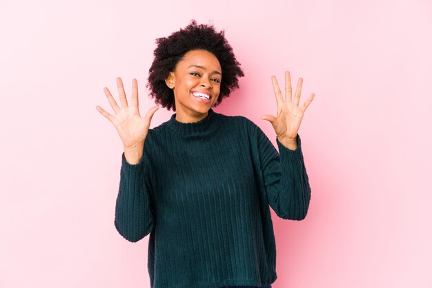 Mittlere gealterte Afroamerikanerfrau gegen einen rosa Hintergrund, der Nr. Zehn mit den Händen zeigt.
