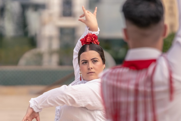 Mittlere Nahaufnahme einer jungen Flamenco-Ballerina, die in Weiß gekleidet ist und mit einem männlichen Tänzer tanzt