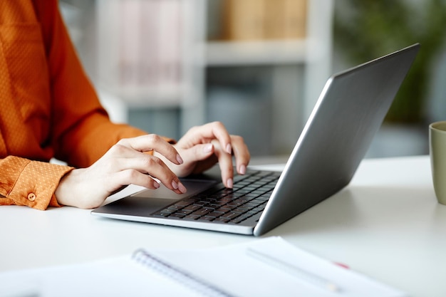 Mittlere Nahaufnahme einer nicht erkennbaren jungen Frau, die im Internet auf einem Laptop im Büro SMS schreibt