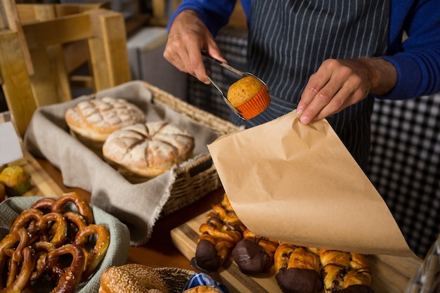 Mittlerer Abschnitt des Personals, der Tasse Kuchen in Papiertüte am Schalter verpackt