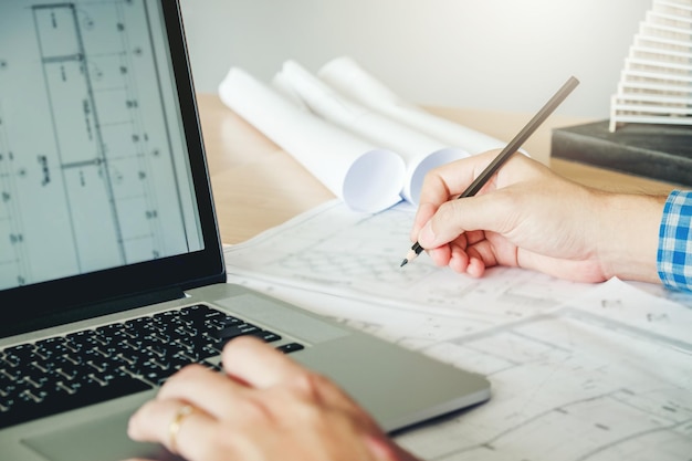 Foto mittlerer abschnitt eines architekten, der mit einem laptop auf eine blaupause schreibt