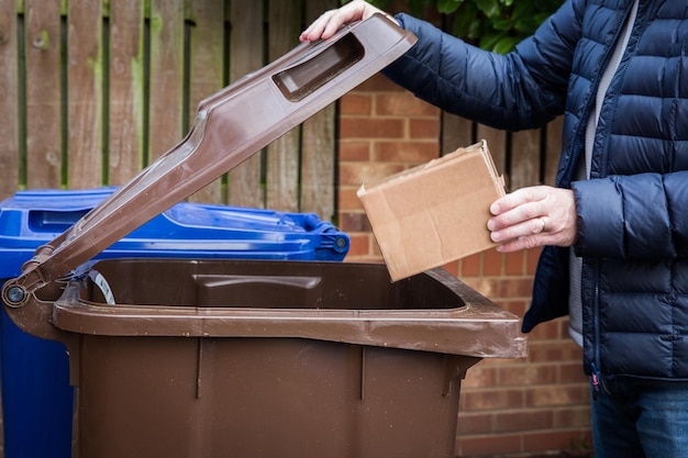 Mittlerer Abschnitt eines Mannes, der eine Kartonbox in einem braunen Recyclingbehälter mit Kopierplatz recycelt