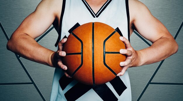Foto mittlerer abschnitt eines sportlers, der einen basketball hält, während er an der wand steht