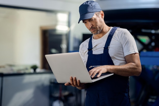 Mittlerer erwachsener Mechaniker mit Laptop in der Autowerkstatt