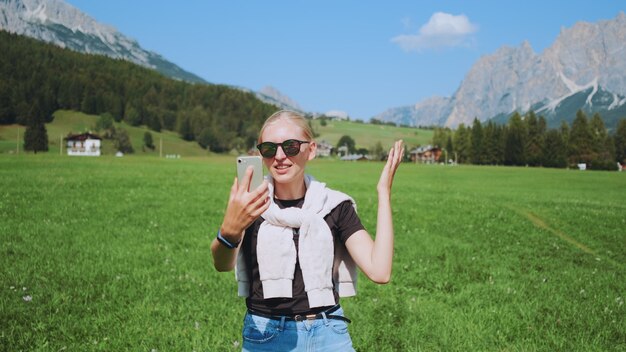 Mittlerer Schuss der Frau, die Videoanruf vom schönen Naturpark vor Bergen macht. Sie teilt Eindrücke von ihrer Reise.