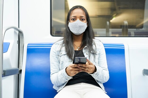 Mittlerer Schuss einer schwarzen Frau, die im U-Bahnwagen sitzt und in eine Kamera schaut, die ein Smartphone hält.