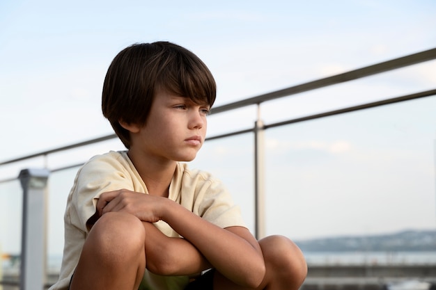 Foto mittlerer schuss trauriger junge, der draußen sitzt