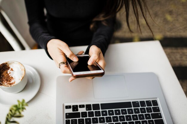 Mittlerer Teil einer Frau, die am Tisch ein Mobiltelefon benutzt
