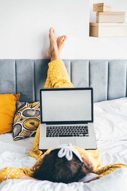 Mittlerer Teil einer Frau, die zu Hause einen Laptop im Bett benutzt