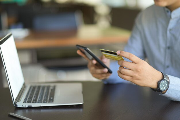 Mittlerer Teil eines Mannes, der ein Mobiltelefon auf dem Tisch benutzt