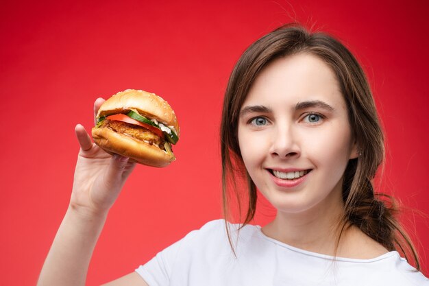 Mittleres Nahaufnahmeporträt der schönen jungen Modefrau, die frisches appetitliches Sandwich beißt. Porträt einer lächelnden, entzückenden Frau, die das Essen von Fast Food im Café genießt?