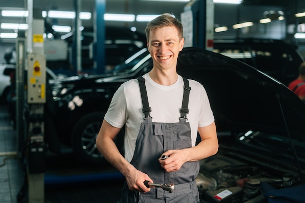 Mittleres Schussporträt eines lächelnden, gutaussehenden jungen Mechanikers in Uniform mit Sonderschlüssel