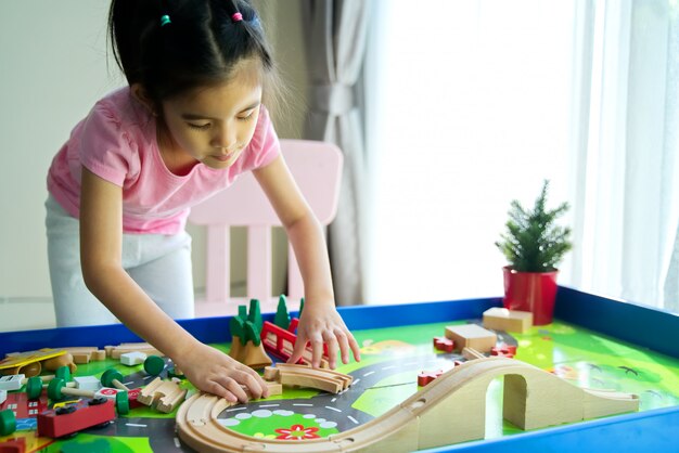 Miúdo bonito asiático pequeno novo que joga o brinquedo de madeira na tabela em casa.