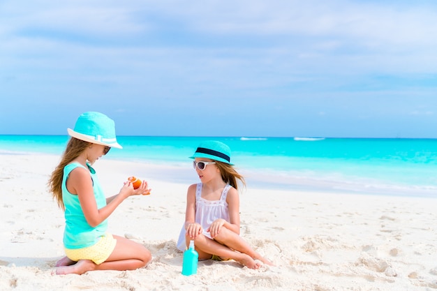 Miúdos que aplicam o creme do sol a se na praia. O conceito de proteção contra radiação ultravioleta