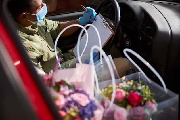 Mixed-Race-Ladenassistent in einem Auto, das mit einem Öko-Stift in der Nähe von Blumen in Taschen auf ein leeres Papier schreibt