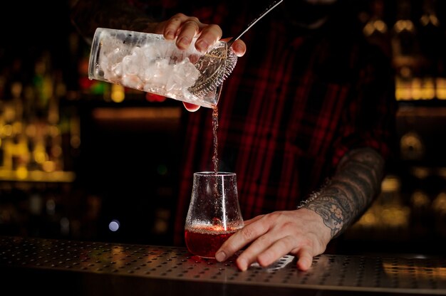 Mixologe gießt frischen und leckeren bittersüßen roten Cocktail in ein leeres Cocktailglas an der Bar