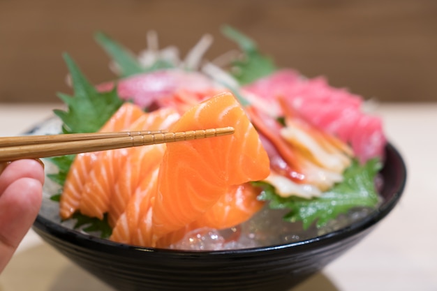 Mixto sashimi de pescado en rodajas sobre hielo en un tazón negro.