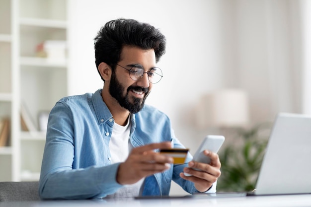 Mobile Banking lächelnder indischer Mann mit Smartphone und Kreditkarte im Büro