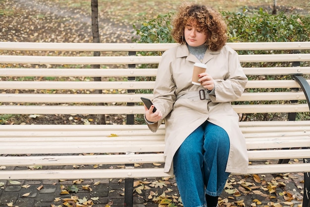 Mobile Kommunikation Herbsttag Gute Zeit Körper positiv Entspannte übergewichtige Frau mit lockigem Haar, die eine SMS auf einer Bank im Park liest