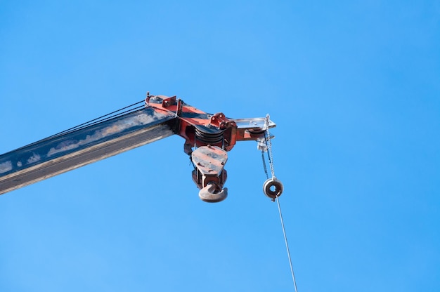 Mobiler Kranausleger mit Haken hängend am Drahtseil Hintergrund blauer Himmel, Nahaufnahme