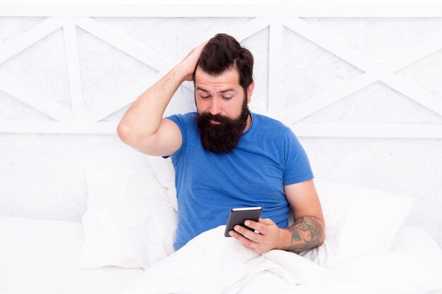 Mobiles Leben durch Telefon Bärtiger Mann benutzt Handy im Bett Hipster überprüft mobile Benachrichtigungen am Morgen Modernes Leben Neue Technologie Mobile Kommunikation und Technologie im Haus