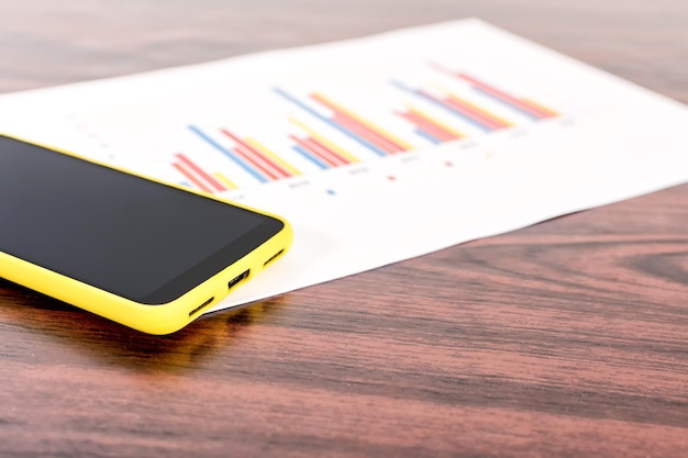 Mobiltelefon mit leerem schwarzem Bildschirm mit Statistikdiagramm auf dem Schreibtisch