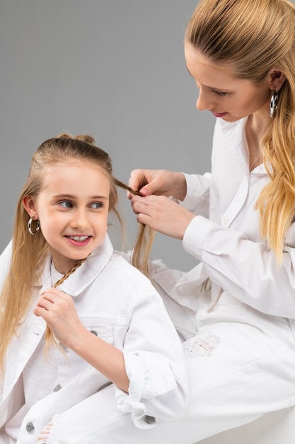 Moça animada de jaqueta branca conversando com a irmã mais velha enquanto ela está ocupada com o penteado