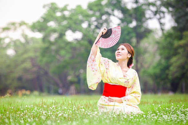 Moça asiática que veste um quimono na grama verde natural.