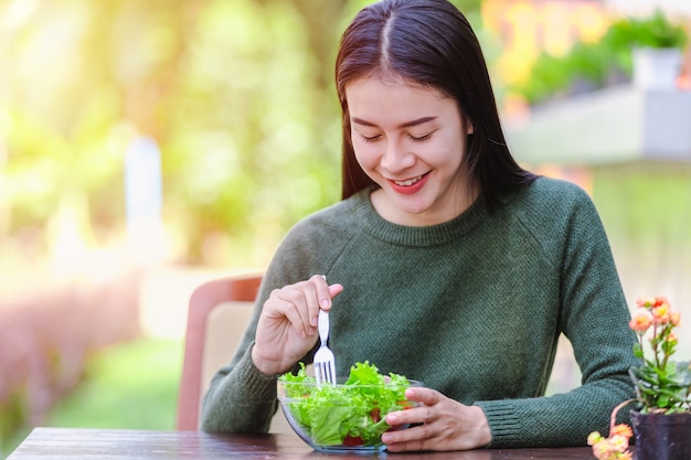 Moça bonita asiática que come o vegetal de salada