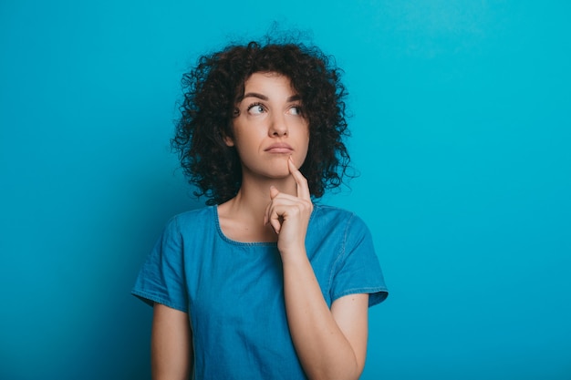 Foto moça bonita com cabelo encaracolado posando com uma camiseta azul sobre um fundo