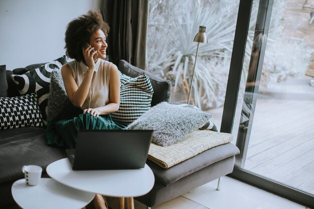 Foto moça bonita com cabelo encaracolado trabalhar no notebook enquanto se senta no sofá em casa