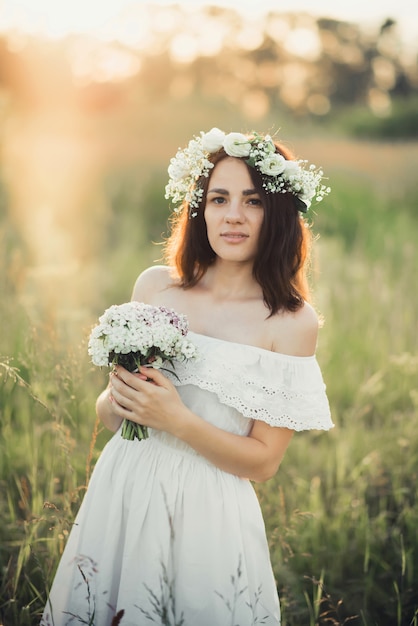 Moça bonita com um buquê de flores e uma coroa de flores em um vestido branco